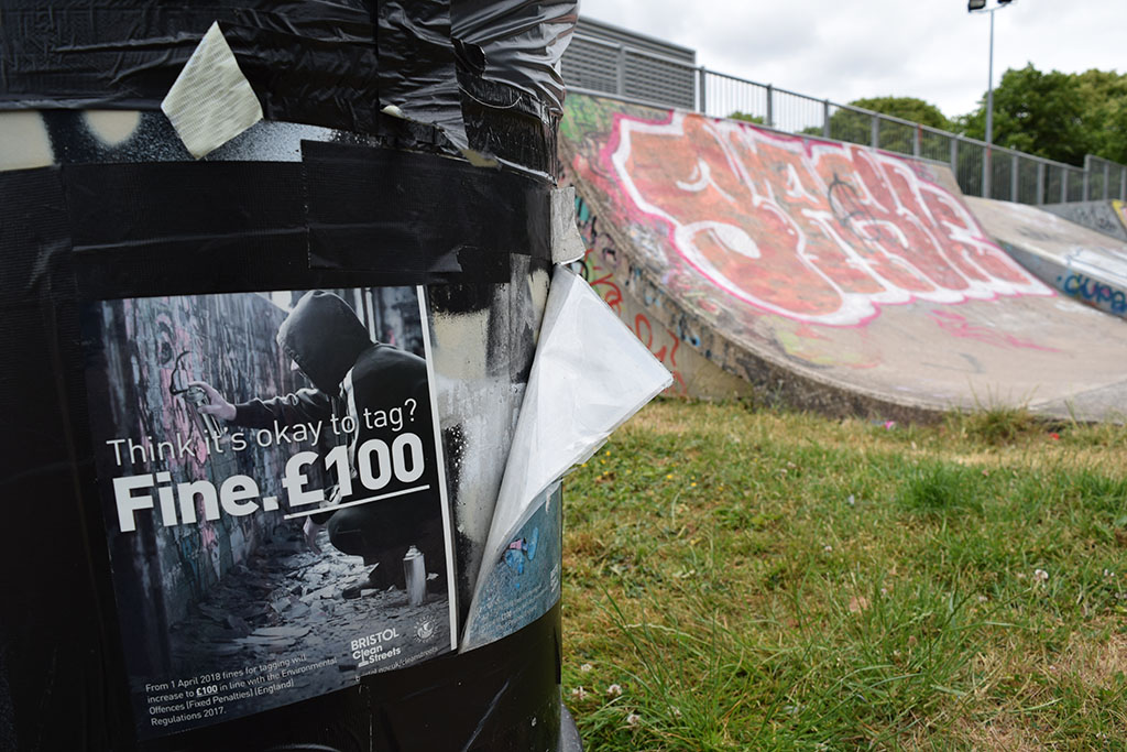 A bin showing an anti-graffiti poster with graffiti in the background